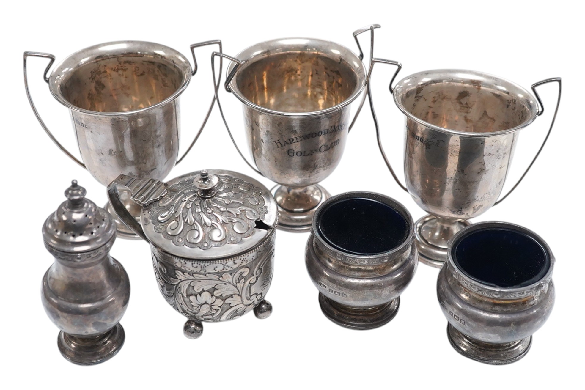 A Victorian repousse silver drum mustard, London, 1887, a silver three piece condiment set, Birmingham, 1936 and a set of three small trophy cups by Mappin & Webb, London, 1925/6. Condition - poor to fair